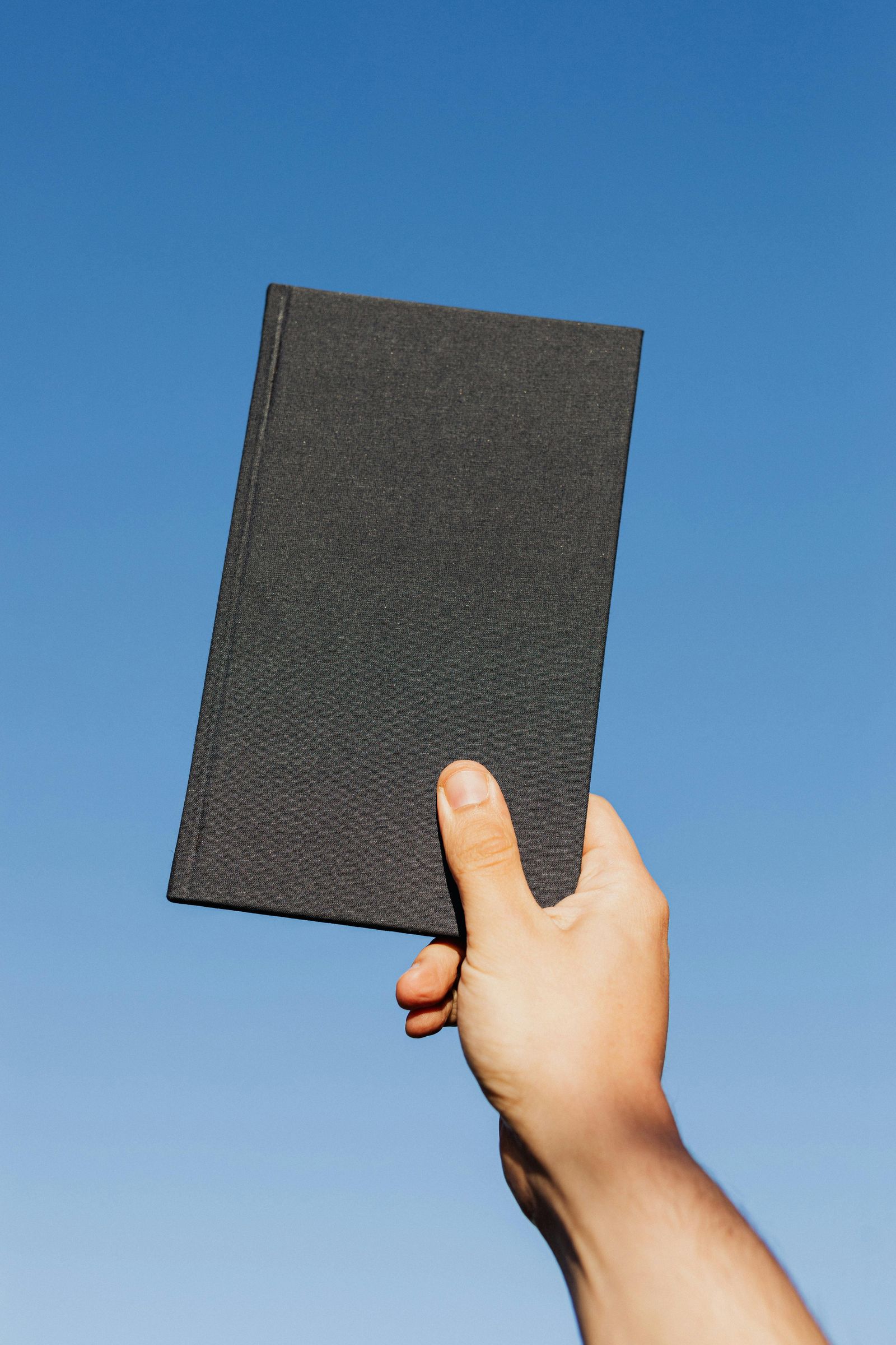 A hand holding a blank black book against a blue background